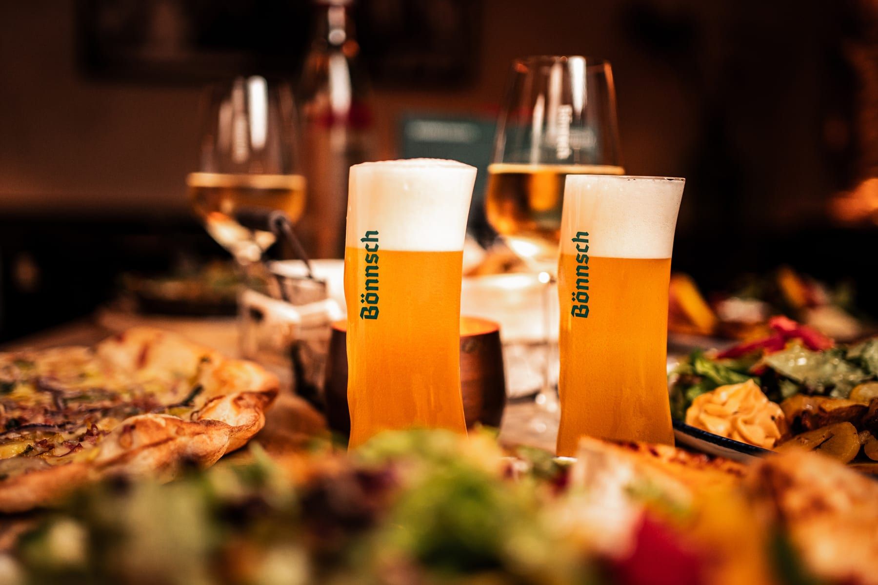 Zwei frisch gezapfte Bönnsch im typischen geschwungenen Bönnsch-Glas auf einem gedeckten Tisch im Brauhaus