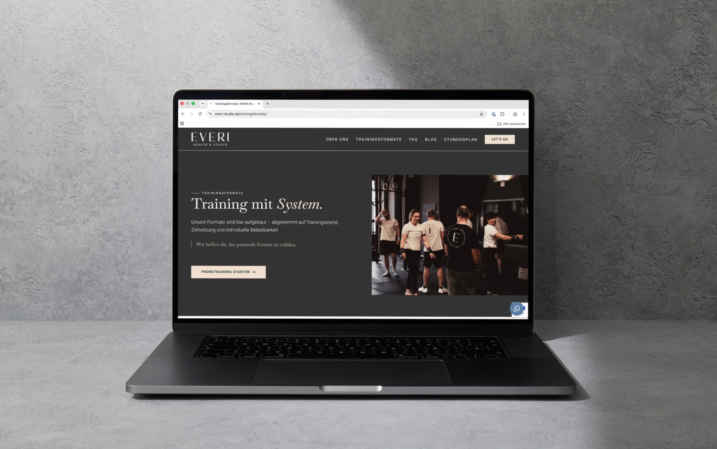 Seite „Trainingsformate“ von everi-studio.de auf einem Laptop vor einer grauen Betonwand