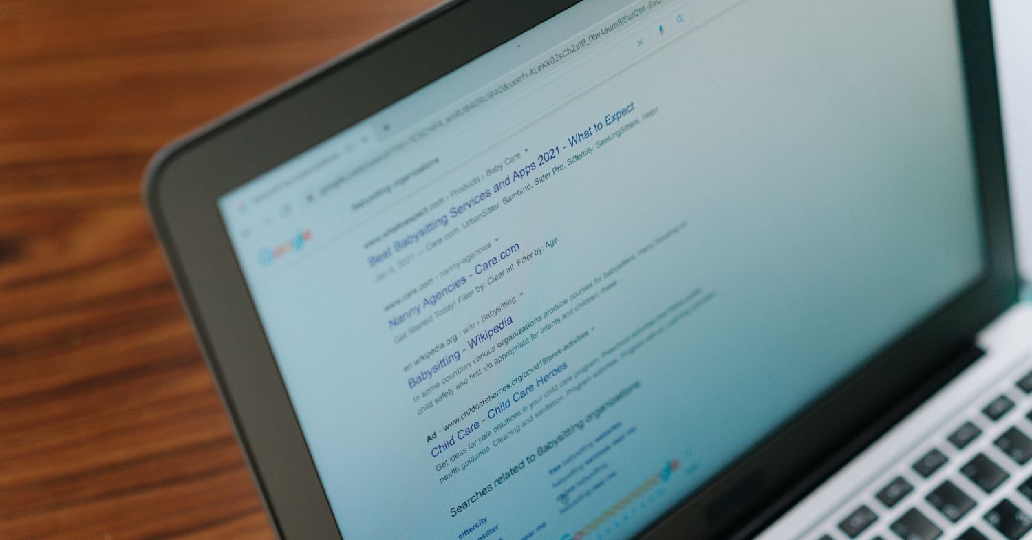 Laptop auf einem Holztisch mit geöffneter Google-Suchergebnisseite, darunter eine als Ad gekennzeichnete Anzeige