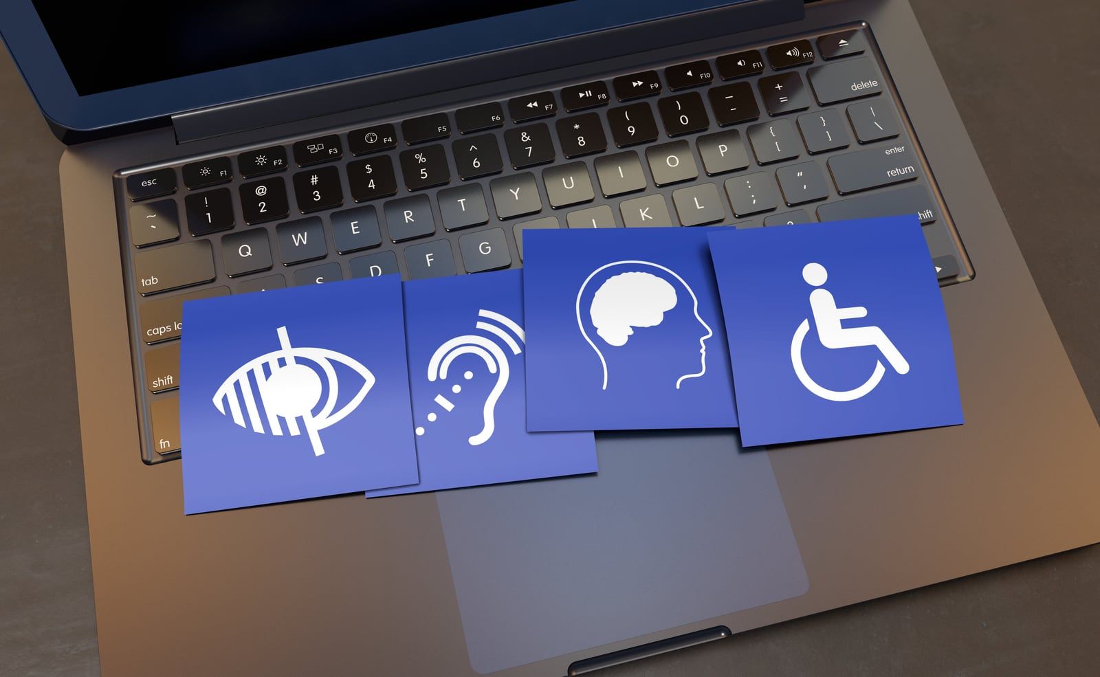 Vier blaue Karten mit Symbolen für Seh-, Hör-, kognitive und körperliche Einschränkungen liegen auf der Tastatur eines Laptops